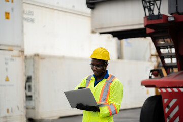 engineer man / worker in safety jumpsuit uniform with yellow hardhat and use laptop computer control at cargo container ship port warehouse.transport import,export logistic industrial service