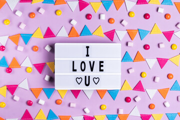 The inscription I love you greeting card for Valentine's Day and Valentine's Day on a white board on a pink background with a multicolored garland holiday