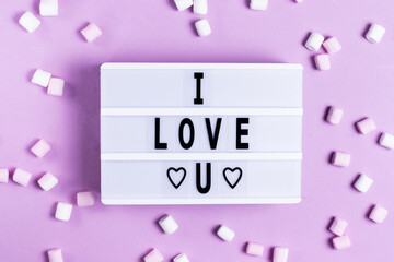 The inscription I love you greeting card for valentine's day and Valentine's day on a white board on a pink background with white and pink marshmallows romantic holiday