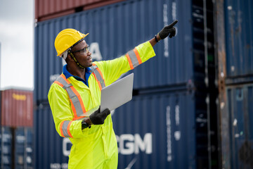 engineer man / worker in safety jumpsuit uniform with yellow hardhat and use laptop computer control at cargo container ship port warehouse.transport import,export logistic industrial service