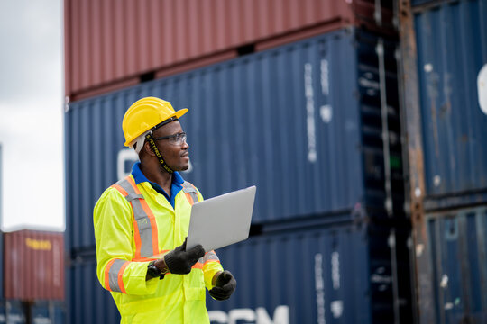 engineer man / worker in safety jumpsuit uniform with yellow hardhat and use laptop computer control at cargo container ship port warehouse.transport import,export logistic industrial service