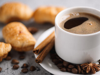 white cup of espresso coffee, coffee beans, cinnamon, with small croissants. Coffee break