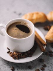 white cup of espresso coffee, coffee beans, cinnamon, with small croissants. Coffee break