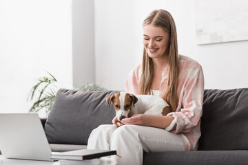 cheerful woman feeding dog with pet food in living room