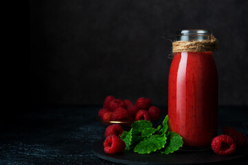 Vegetarian raspberry smoothie in a glass bottle on a dark background, close-up