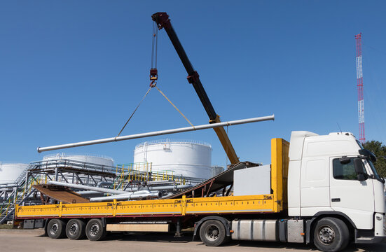 The crane unloads the metal pipe from the truck body