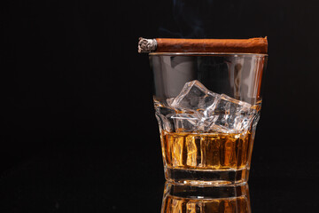 Burning cigar and glass of whisky on black background