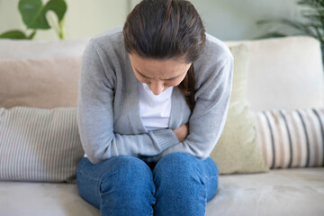 Young woman suffering PMS pain on sofa.