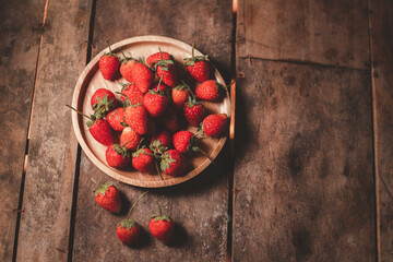 Delicious red strawberry fruit clusters placed on a plate with a wooden background.