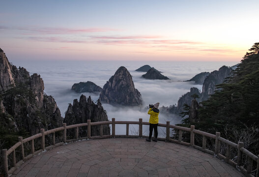 The girl holding camera for taking photo with the scenery view of the Huangshan mountain, and cloud scape in the morning time winter season