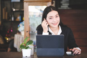 Businesswoman in formal suit wearing wireless earphone and working with tablet computer at modern cafe.