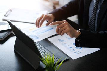 Close up view of businessman working on tablet computer with financial business graph information diagram on office desk.