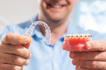 Dental care.Smiling orthodontist doctor holding aligners and braces in hand shows the difference...