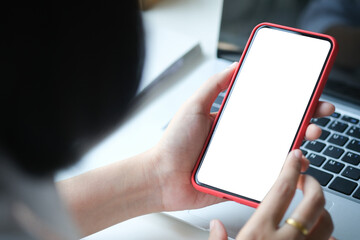 Close up view of young woman hands holding mock up smart phone with blank white screen at her workspace.