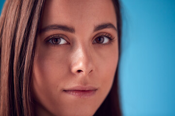 Portrait Of Confident Woman With Serious Expression Looking Into Camera Against Blue Background