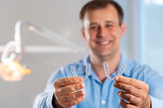 A smiling dentist doctor holds transparent aligners in his hands