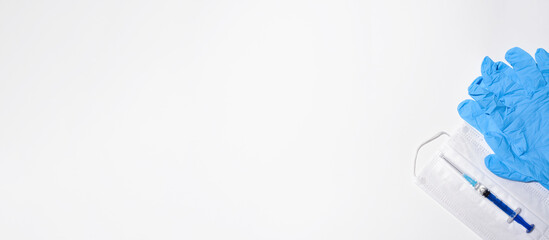 Medical face mask, syringe and blue gloves on a white background, flat lay. Banner equipment for vaccination against disease, copy space