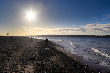 Silhouettes of people talking a walk on a sunny baltic sea beach in Germany.