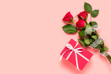 Bouquet of three red roses and gift box with white bow knot on pink background. Mother's, women's or Valentine's day greeting. Love and dating concept. Flat lay, copy space for text on left side