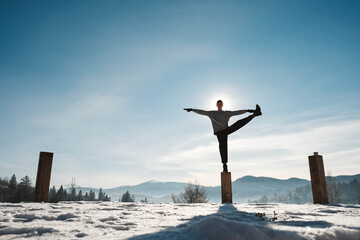 Silhouette of a man doing yoga exercises in front of amazing sunset on the winter mountains. Copy, empty space for text