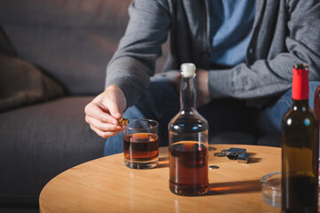 cropped view of man holding wedding ring near glass and bottle of whiskey, blurred background