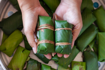Hand holding raw steamed sticky rice with banana or Thai people call Khao Tom Mud which is being prepared to steam.