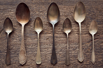 Seven empty alpacca vintage spoons on a wooden background, top view