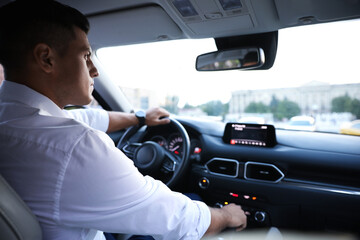 Handsome man driving his modern luxury car, view from backseat