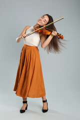 Beautiful woman playing violin on grey background © New Africa
