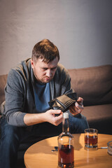drunk man holding empty wallet near bottle and glass of whiskey at home