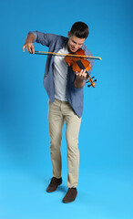 Happy man playing violin on light blue background © New Africa