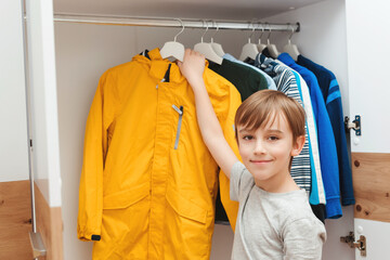 Boy taking jacket from hanger stand. Wardrobe with child's clothing.