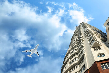 Fototapeta na wymiar Airplane flying in blue sky over skyscraper