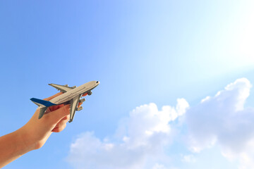 close up photo of man's hand holding toy airplane against blue sky with clouds. filtered image