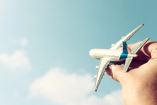 close up photo of man's hand holding toy airplane against blue sky with clouds. filtered image