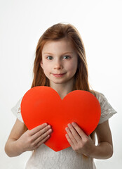 Portrait of smiling red-haired little girl holding big red heart in her hands on white background. Love, Valentines Day, Mothers Day or Fathers Day concept.