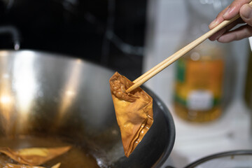 Action of human hand is using chopsticks to cooking the dried dumpling with background of kitchen pan. Close-up and selective focus, food photo.