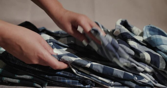 Women's hands correct a stack of men's shirts on the shelf