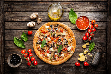 Tasty vegetable pizza and cooking ingredients tomatoes and basil on wooden background. Top view