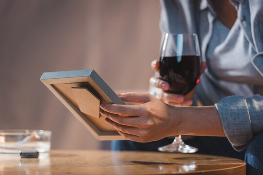 cropped view of woman holding glass of red wine and photo frame on blurred background