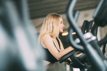 portrait of fitness young woman in sports clothing  and exercising on bicycle at the fitness center