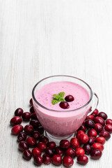 Pink smoothie with cranberry in glass cup on white wooden table