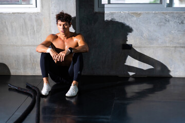 Obraz premium sportsman taking a break after training with battle rope at the gym sitting and drinking water at sport club. Fitness Healthy lifestye and workout at gym concept.