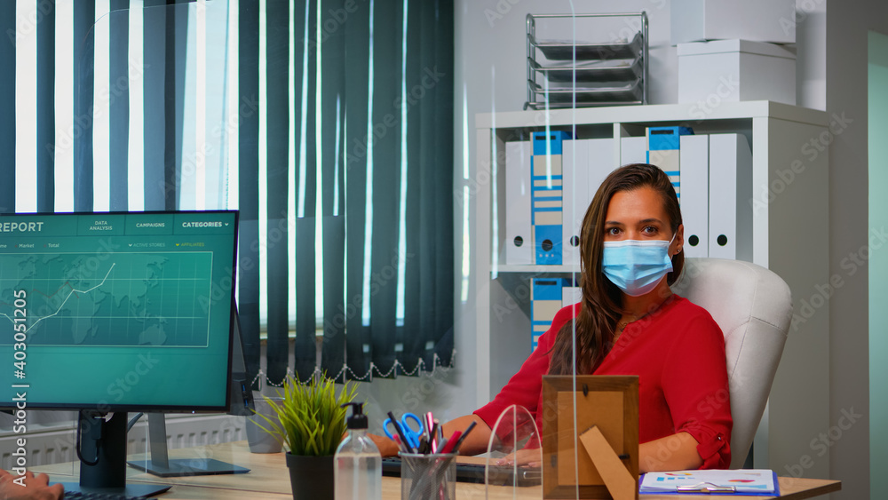 Poster woman with protection mask working and looking at camera sitting in front of pc. employees in worksp