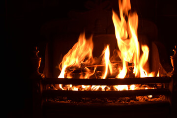 Closeup of dancing flames with dark background of burning wooden logs in fireplace, warming light in Christmas holidays