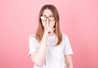 Young girl on a pink background asking for silence with a finger on her lips. Silence and secret concept.