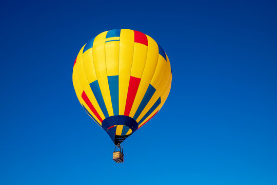 Bright multicolored yellow and red hot air balloon with basket against blue sky