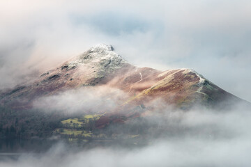 Lake District mountain Catbells covered in low lying misty cloud. Snowcapped moody fell tops.