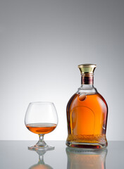view of glass of cognac and a bottle aside on grey  background. 