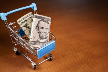 Small shopping cart with US Dollars in it.. Concepts about online shopping that consumers can buy things directly from their home or office just using a few clicks via web browser.